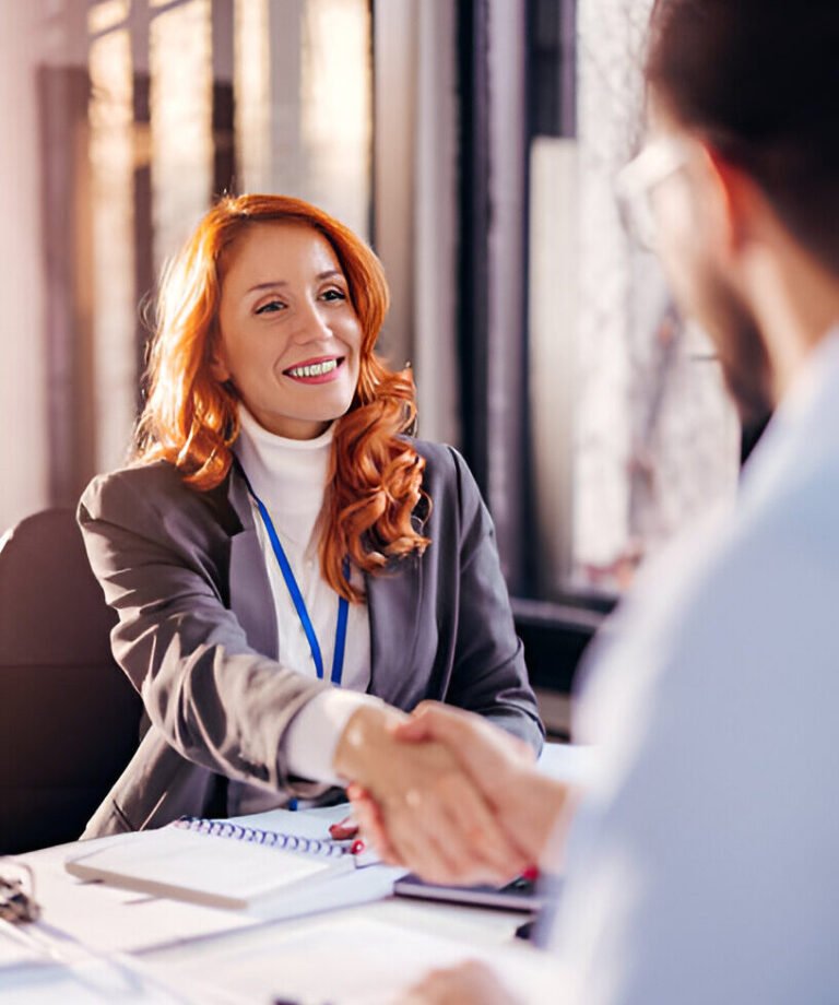 A young woman smiling and shaking hands with a client after finalizing a real estate contract in the San Francisco Bay Area.