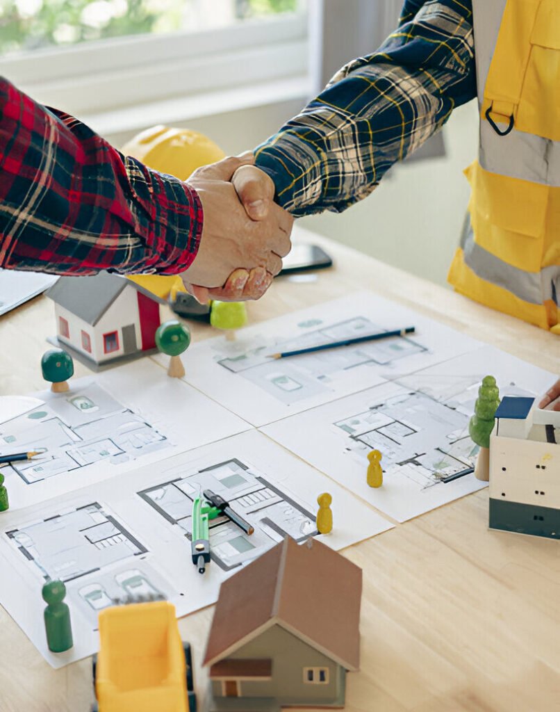 A yellow hard hat on a table with house design blueprints and a construction team discussing infrastructure repairs for older homes in the San Francisco Bay Area.
